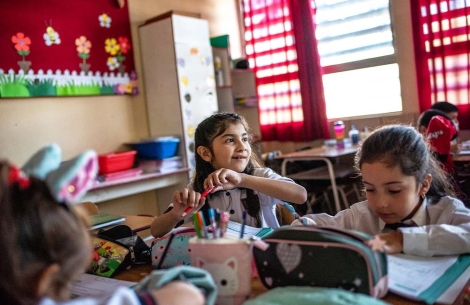 A smiling Aylen sits at her school desk