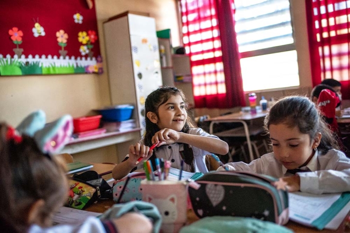 A smiling Aylen sits at her school desk