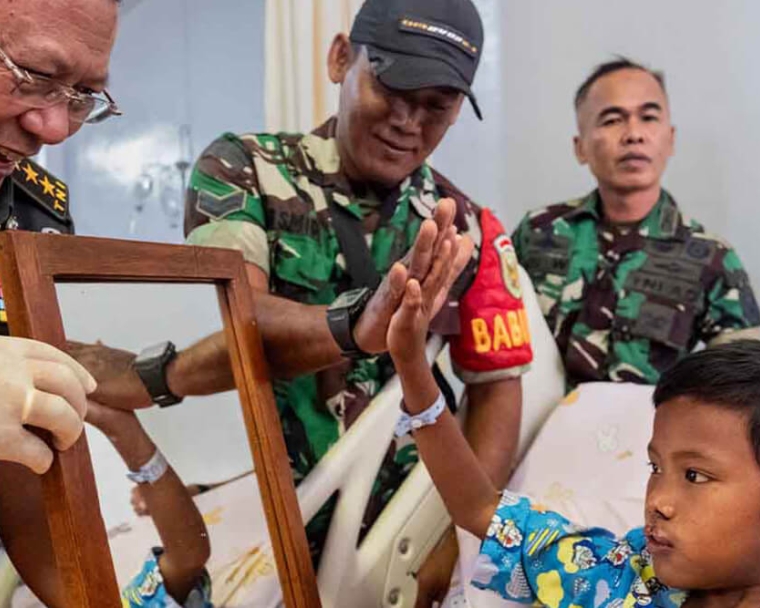 Soldados indonesios sonríen y chocan las manos con Rajib mientras se mira en el espejo tras su cirugía de fisura labio palatina